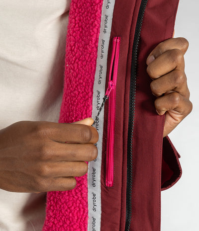 *MALE* Close-up of a person's hands demonstrating a zipper feature on a burgundy Dryrobe jacket with a bright pink fleece lining.