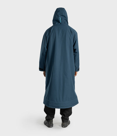 *MALE* A person viewed from the back wearing a long hooded coat in a muted blue-teal color, paired with black pants and dark shoes, against a light gray studio background.