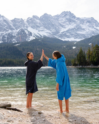 Two people in towel robes giving a high-five by a lake with mountains in the background