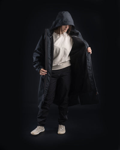 *FEMALE*Person wearing a long black coat with a hood on a black background