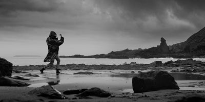 Person in camouflage walking on a rocky beach with a stormy sky
