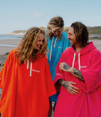 Three people wearing colorful dryrobe towel robes on a beach.