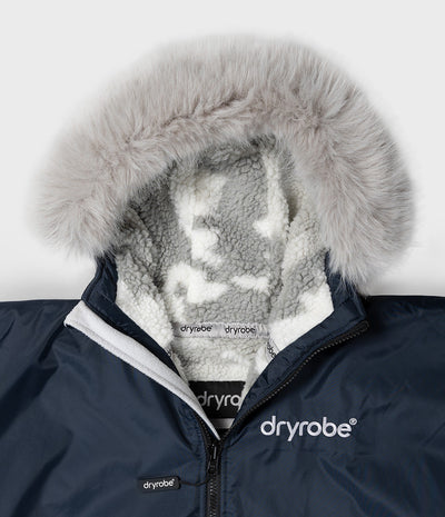 *MALE* Close-up of a navy blue Dryrobe hooded jacket with a fluffy light gray faux-fur trim and a white sherpa lining, showing the Dryrobe brand on the chest and collar.