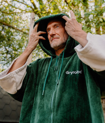 *MALE* Person wearing a green 'dryrobe' hooded garment with trees in the background