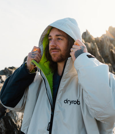 *MALE* Person wearing a white Dryrobe with 'dryrobe' branding in a natural setting.
