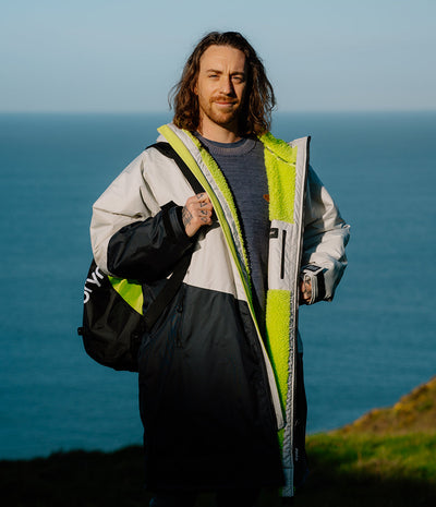 *MALE* Man wearing a reflective Dryrobe with a backpack against a scenic ocean backdrop
