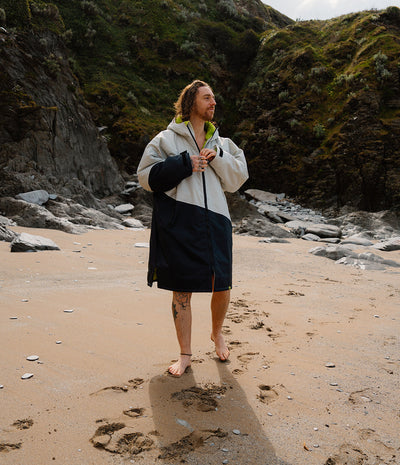 *MALE* Person standing on a beach with a scenic background of rocks and greenery