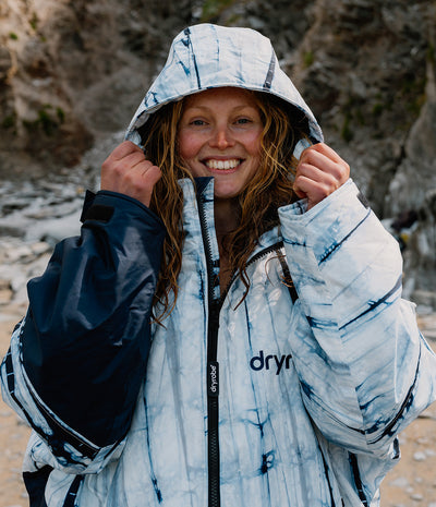 Person wearing a blue and white patterned Dryrobe with a hood, standing outdoors.