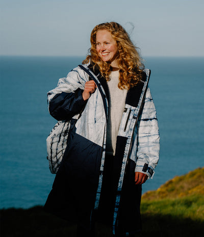 Person wearing a patterned Dryrobe standing on a cliff overlooking the ocean.