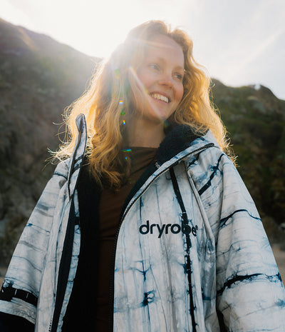 Person wearing a 'dryrobe' jacket outdoors with mountains in the background