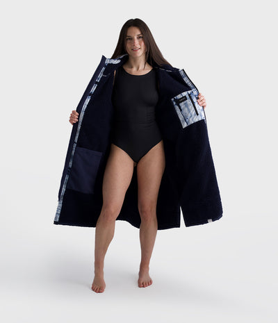 Woman wearing a long dark blue Dryrobe with patterned pockets on a white background