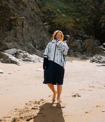 Woman standing on a beach with rocky cliffs and greenery in the background