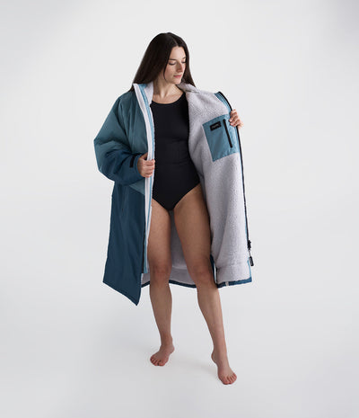 Woman holding a large blue and gray Dryrobe over her shoulders on a white background