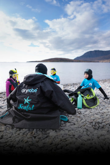 People sitting on a rocky shore with 'Dryrobe' branded jackets and gear.