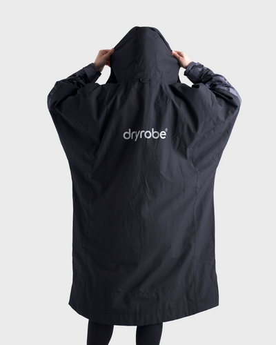 *MALE*Person wearing a black dryrobe jacket with the brand logo on a light grey background