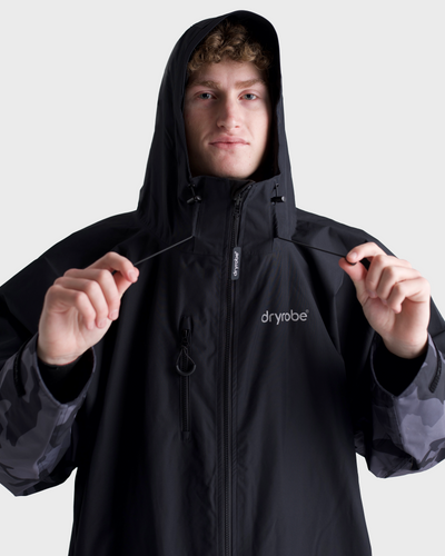 *MALE*Person wearing a black hooded jacket with 'dryrobe' branding on a light gray background