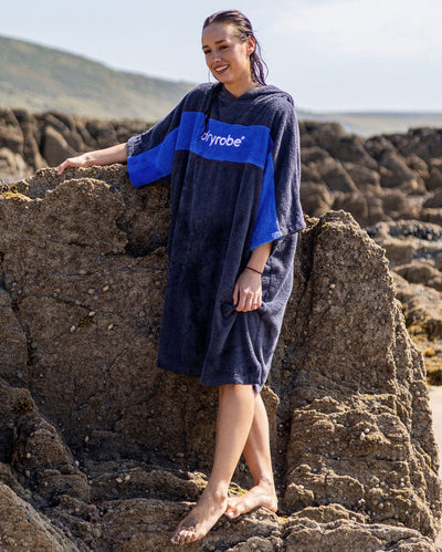 Woman with wet hair stood by rocks, wearing Organic Towel dryrobe Remix in Navy Royal Blue