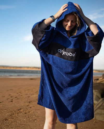 Woman stood on a beach wearing Organic Towel dryrobe Remix in Royal Blue Navy with hood up