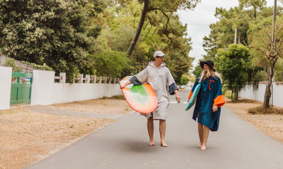 Two people walking on a path outdoors, each carrying a colorful surfboard under a clear sky.