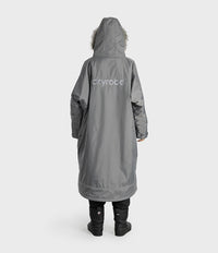 A person shown from the back wearing a long gray hooded dryrobe with a white 'dryrobe' logo on the back, black pants, and black boots against a light gray studio background.