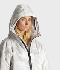 A woman wearing a light gray hooded Dryrobe with a subtle white camouflage pattern, black zipper, and a visible 'dryrobe' logo on the chest, set against a plain light gray background.