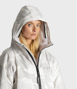 A woman wearing a light gray hooded Dryrobe with a subtle white camouflage pattern, black zipper, and a visible 'dryrobe' logo on the chest, set against a plain light gray background.