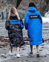 Two people walking along beach with their backs to the camera, wearing dryrobe Advance Long Sleeve REMIX Range change robes