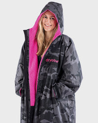 Close up of woman smiling wearing dryrobe Advance Long Sleeve REMIX Range change robe in Black Camo Pink Black with hood up 