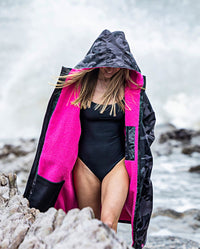 Woman walking along beach, wearing dryrobe Advance Long Sleeve REMIX Range change robe in Black Camo Pink Black