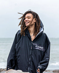 Man stood on a beach wearing Black Grey Camo dryrobe Advance Long Sleeve REMIX Range