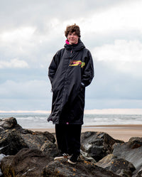 Man stood on a beach wearing Black Pink Camo dryrobe Advance Long Sleeve REMIX Range