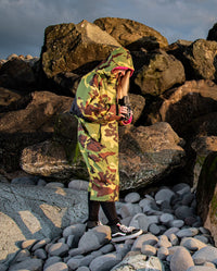 Woman stood by rocks on beach, wearing dryrobe Advance Long Sleeve REMIX Range change robe in Camo Pink Black