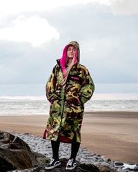 Woman stood on rock in front of the sea, wearing dryrobe Advance Long Sleeve REMIX Range change robe in Camo Pink Black