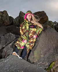 Woman sat on rocks, wearing dryrobe Advance Long Sleeve REMIX Range change robe in Camo Pink Black