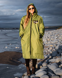 Woman stood on the beach in the sun, wearing dryrobe Advance Long Sleeve REMIX Range change robe in Forest Green Black Camo