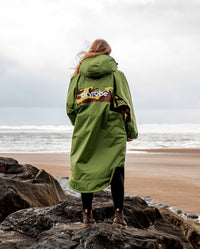 Woman stood facing out to sea with back to camera, wearing dryrobe Advance Long Sleeve REMIX Range change robe in Forest Green Black Camo