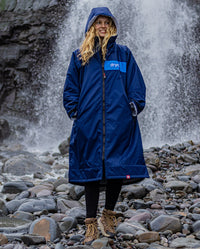 Woman stood in front of waterfall, wearing dryrobe Advance Long Sleeve REMIX Range change robe in Navy Grey Cobalt 