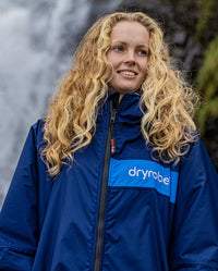 Close up of woman stood in front of waterfall, wearing dryrobe Advance Long Sleeve REMIX Range change robe in Navy Grey Cobalt 