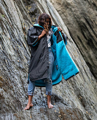 Woman stood on top of rocks on a beach, wearing Black Blue dryrobe® Advance Short Sleeve