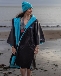 Woman stood in front of the sea in swimming costume, wearing Black Blue dryrobe® Advance Short Sleeve