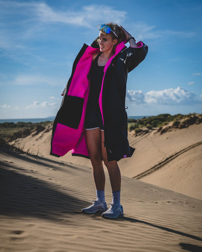 Woman stood in running gear in sand dunes, wearing Black Pink dryrobe® Advance Short Sleeve unzipped