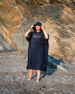 Woman stood on a beach wearing Navy Blue Organic Towel dryrobe® with hood up