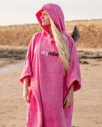 Woman stood on a beach wearing Pink Organic Towel dryrobe® with hood up