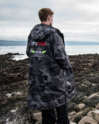 Man stood with back to the camera on a beach, wearing OCR dryrobe® Advance Limited Edition change robe 