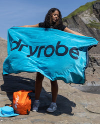 Woman stood on a beach, holding up Blue Charcoal Grey dryrobe® beach towel 