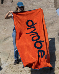 Woman stood on a beach holding Orange dryrobe® Beach Towel  