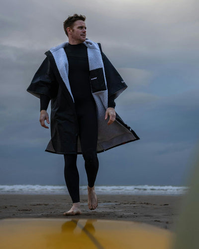 Adult male on beach wearing Dryrobe® black grey remix