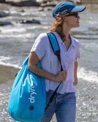 Woman walking on beach, carrying dryrobe Compression Travel Bag in Blue on shoulder