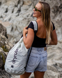 Woman smiling on beach, holding dryrobe Compression Travel Bag in Stone