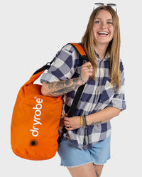 Woman smiling carrying dryrobe Compression Travel Bag in Orange on shoulder